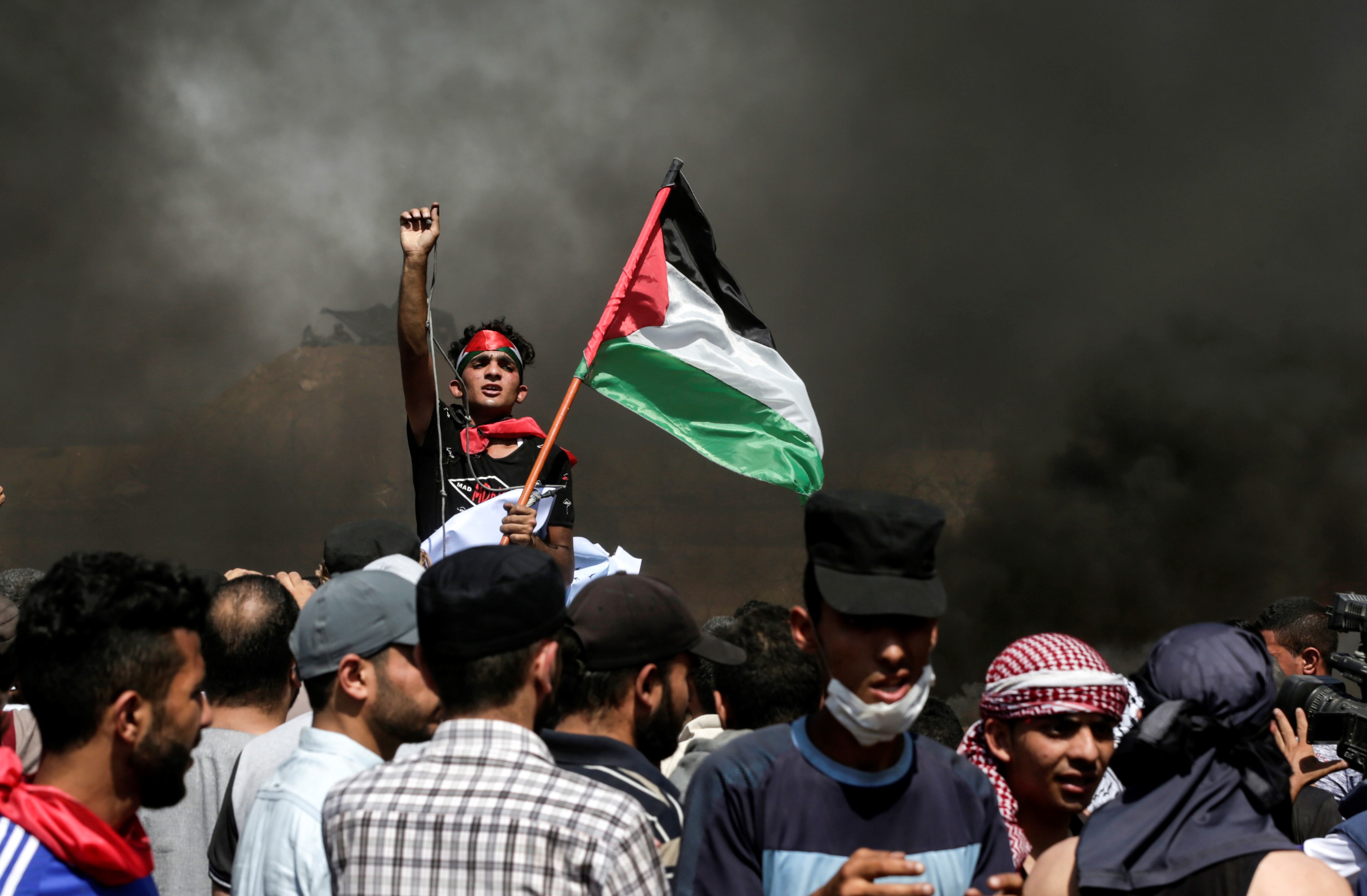  A Palestinian protester waves his national flag as smoke billows from burning tyres during a demonstration along the border between the Gaza strip and Israel on 8 June, 2018 (AFP)