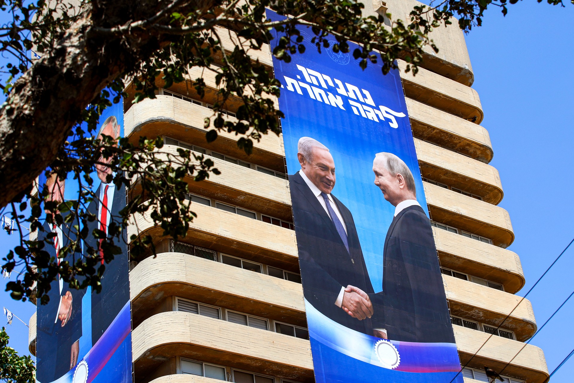 Two giant election banners hanging from a building show Benjamin Netanyahu shaking hands with Donald Trump and Russian President Vladimir (AFP)