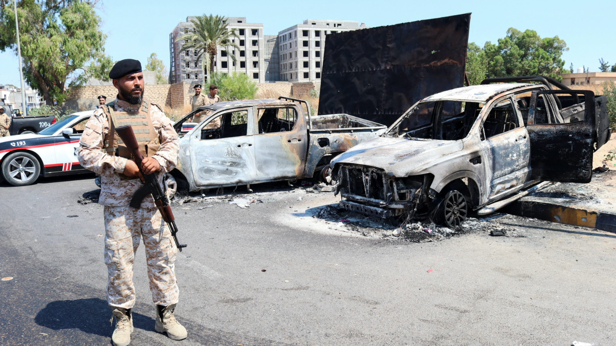 Un miembro de la unidad armada libia Brigada 444 frente a vehículos quemados en el área de Ain Zara en Trípoli el 22 de julio de 2022 (Reuters)