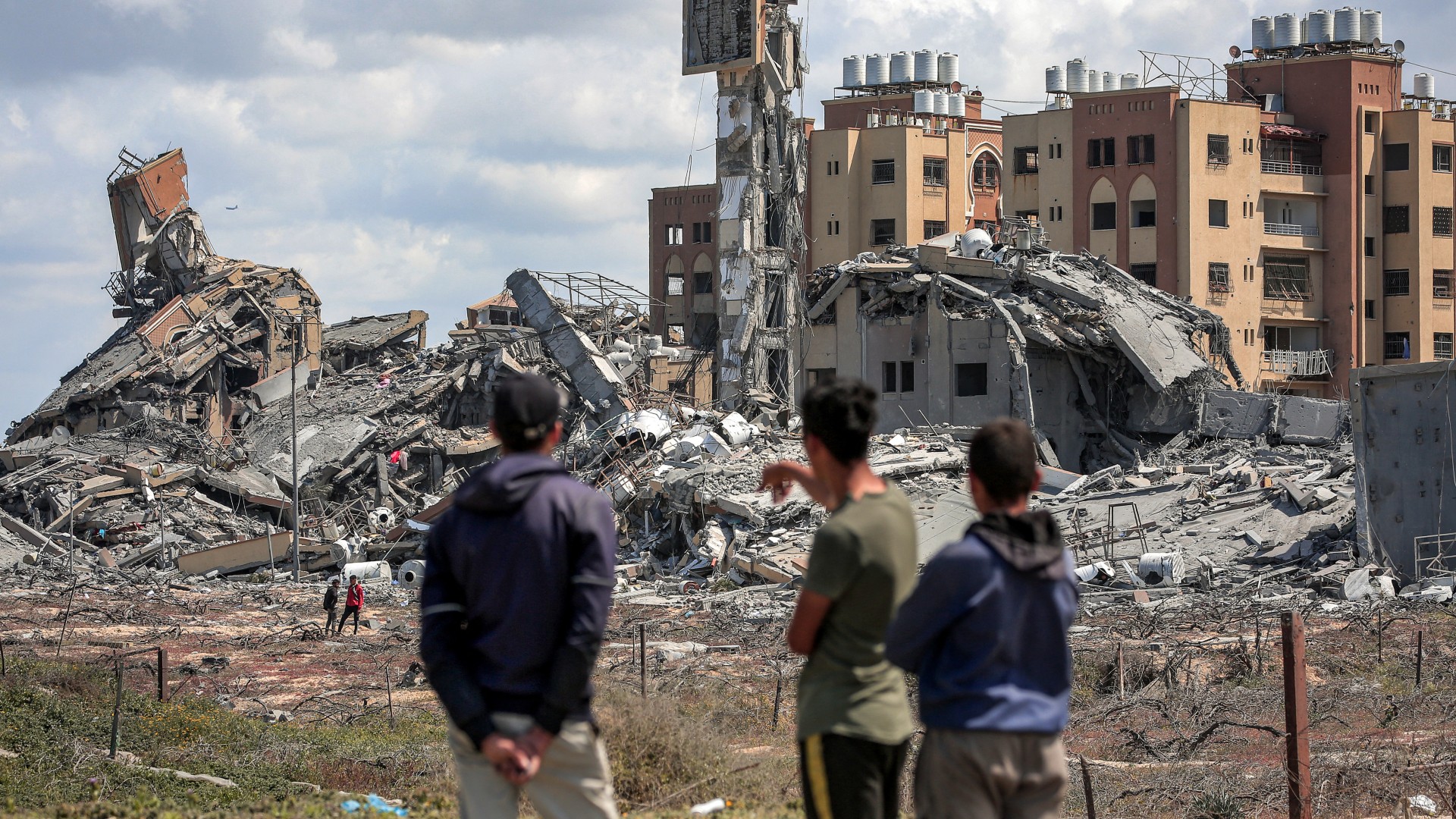 Des jeunes Palestiniens observent au loin les décombres des bâtiments détruits dans le quartier résidentiel d’Asra, au nord-ouest de Nuseirat, dans la bande de Gaza, le 25 mars 2024 (AFP)