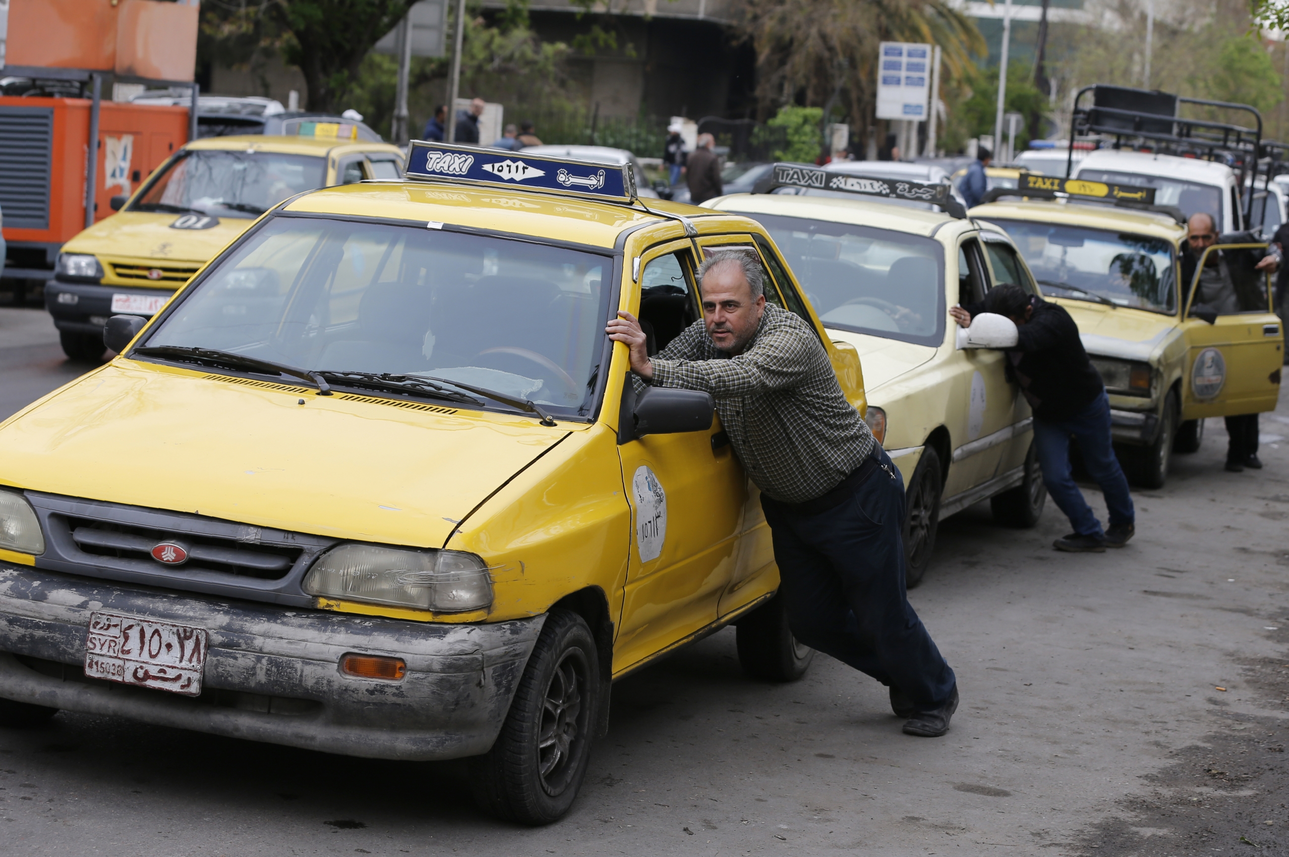 Taxi drivers push their cars that ran out of gasoline to a petrol station in the Syrian capital Damascus on April 16, 2019.
