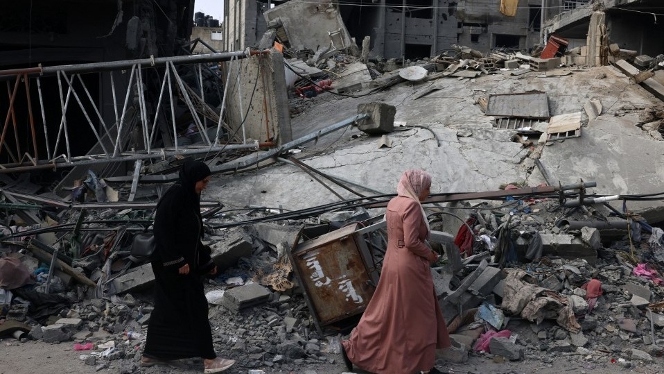 Women walk past a destroyed building in the aftermath of Israeli bombing in Rafah in the southern Gaza Strip on 28 October 2023 (AFP)