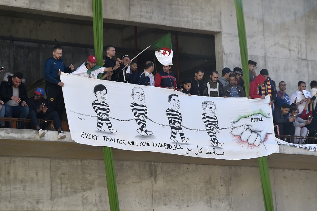 Algerians display a banner showing, from left. Said Bouteflika, Abdelmadjid Sidi Said, General Secretary of the General Union of Algerian Workers (UGTA), Algeria's Forum des chefs d'entreprises (FCE) chairman Ali Haddad, and Algerian former Prime Minister Ahmed Ouyahia in chain, as they demonstrate during the first Friday rally since the president's surprise announcement this week that he would not seek re-election (AFP)