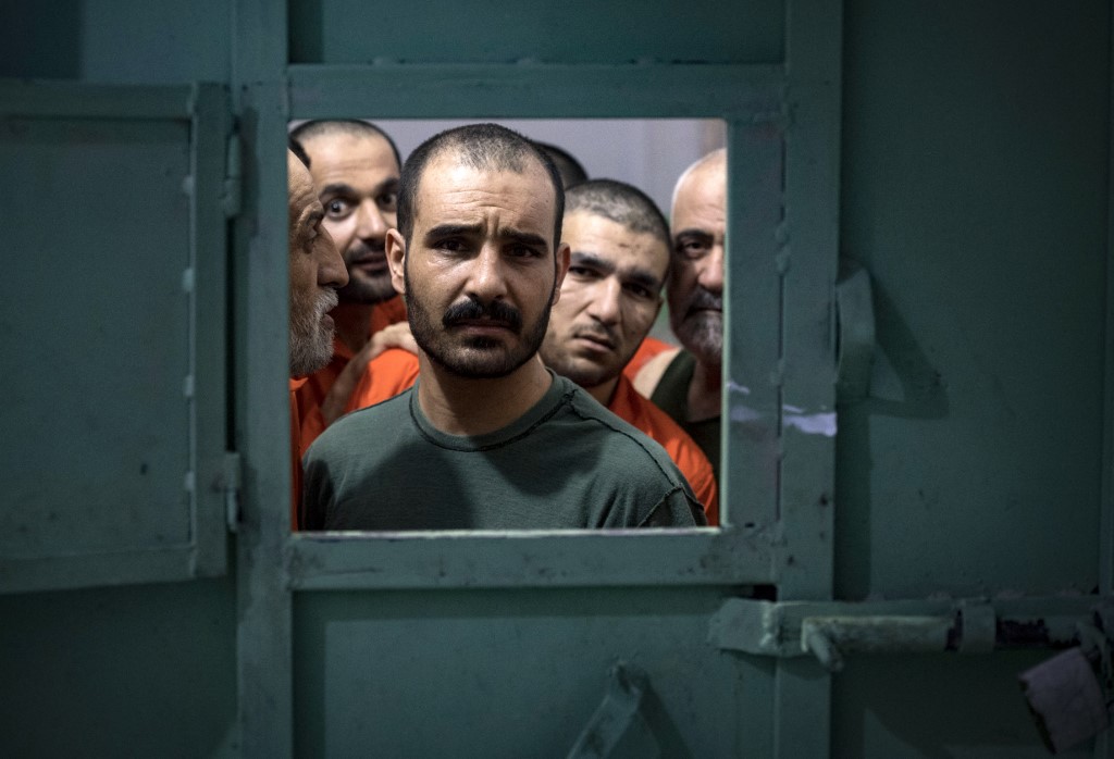 Des hommes soupçonnés d'être affiliés au groupe État islamique (EI), regardent par l'ouverture d'une cellule de prison dans la ville de Hassaké, le 26 octobre 2019 (AFP/Fadel Senna)