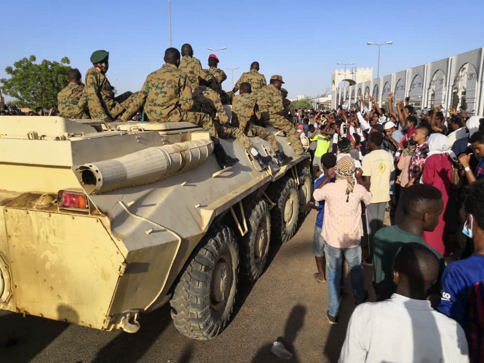  Sudanese protesters flash the victory sign at a passing military vehicle as they rally for a second day outside the military headquarters in the capital Khartoum on 7 April (AFP)