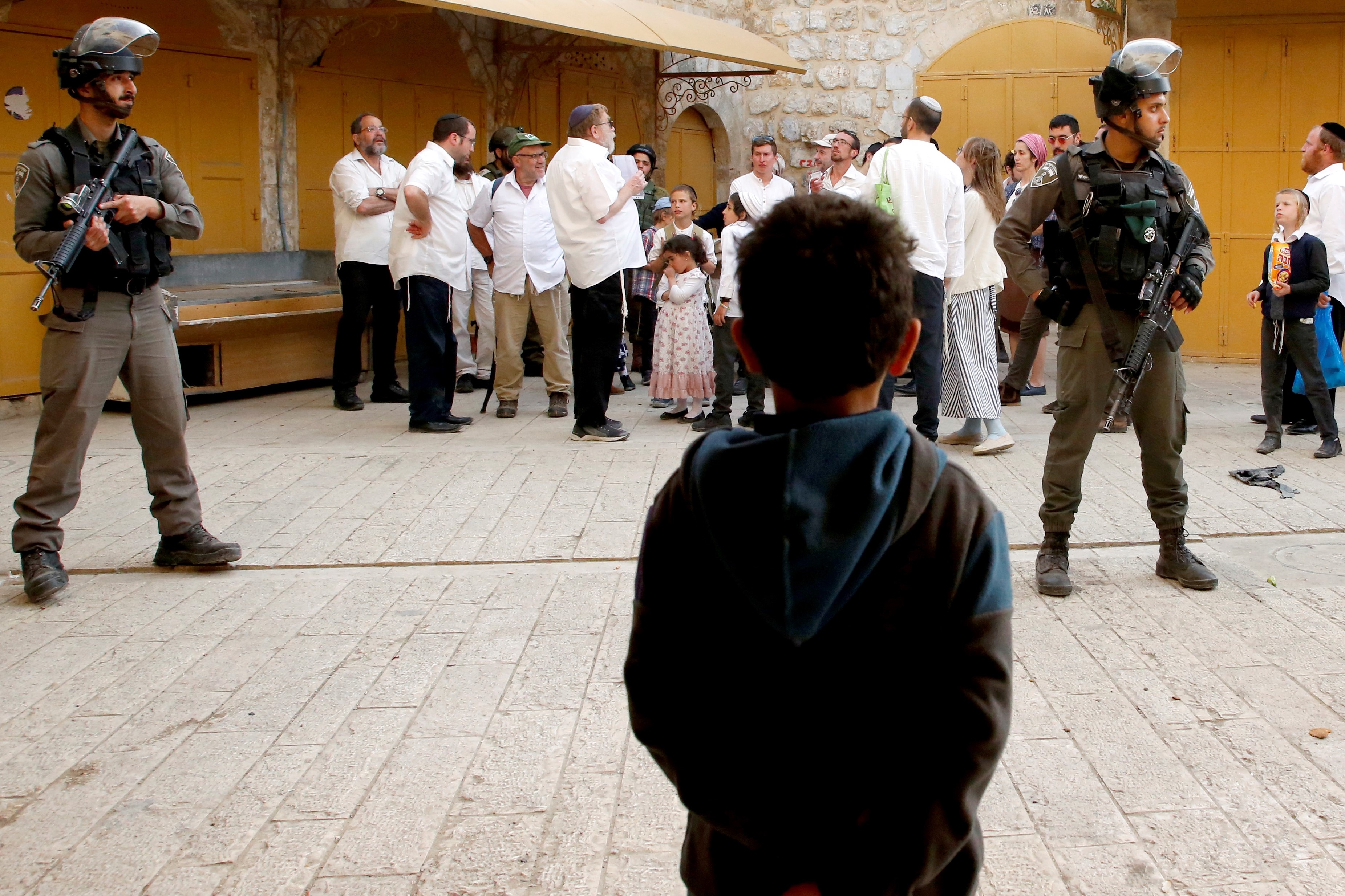 A Palestinian child looks at Israeli soldiers standing guard as settlers stroll through the market in Hebron on 13 April (AFP)
