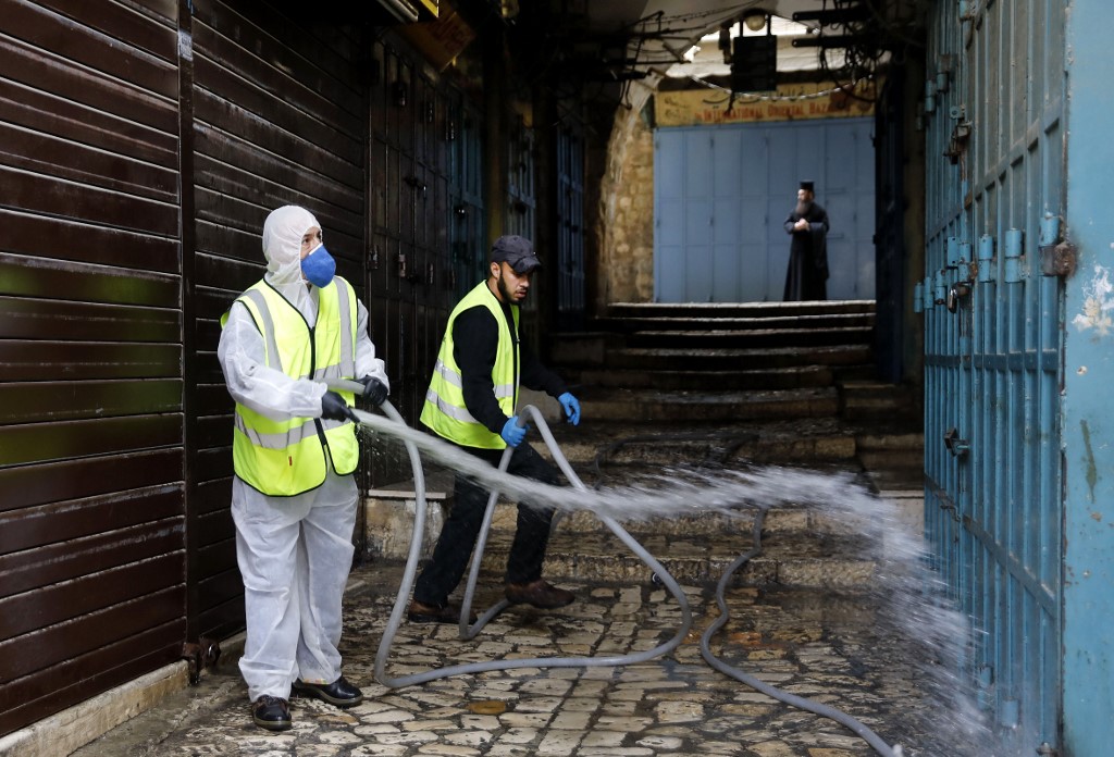 Des employés municipaux désinfectent une ruelle menant à l’église du Saint-Sépulcre, dans la vieille ville de Jérusalem, après sa fermeture pour les non-résidents afin de contenir la propagation du nouveau coronavirus, le 30 mars 2020 (AFP)