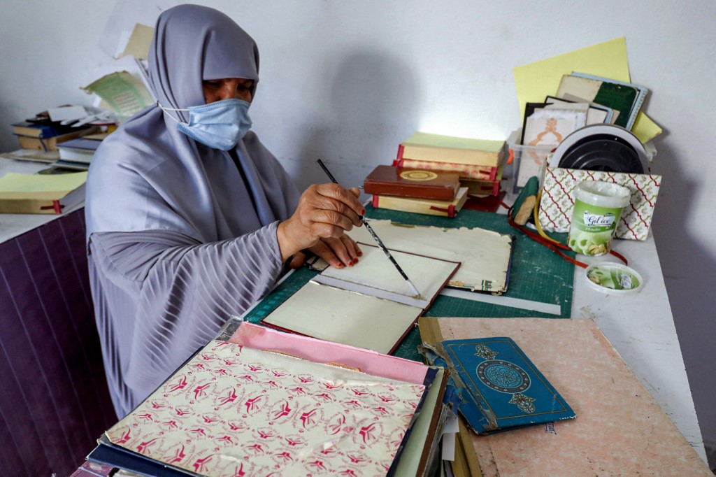 Une femme place de la colle avec un pinceau sur la reliure rigide d’un volume du Saint Coran, lors d’un atelier sur la restauration de ses copies à Tripoli, la capitale libyenne, le 22 mars 2022 (AFP/Mahmoud Turkia)