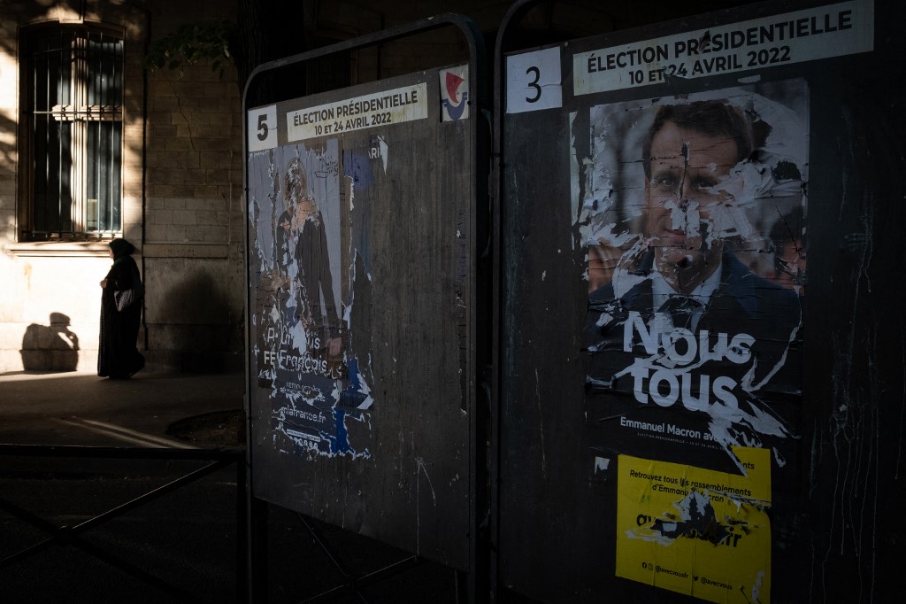 À Paris, une femme musulmane passe devant des affiches des deux finalistes à la présidentielle le 21 avril 2022  (AFP/Joël Saget)