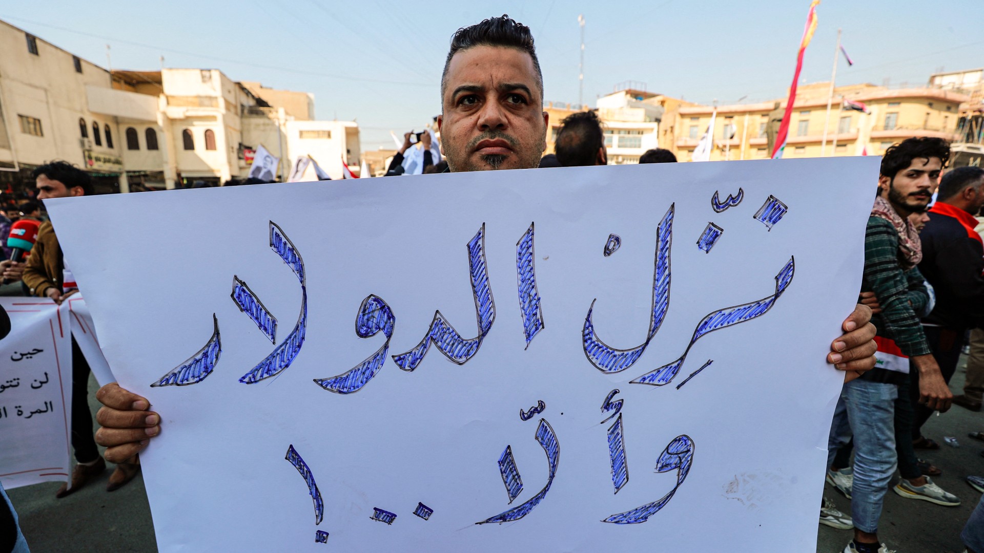 A man stands holding a sign reading "depreciate the rate of the dollar, or else..!" during a protest outside the Central Bank in Baghdad (AFP)