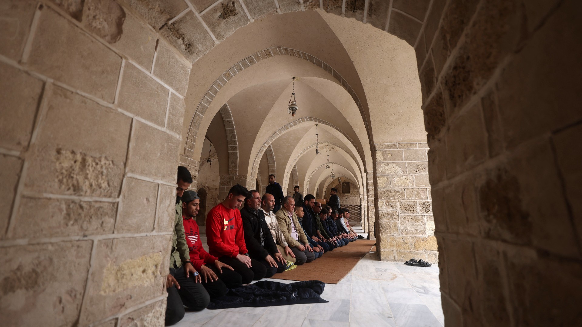 A row of men can be seen praying inside the stone archways of the Omari mosque.