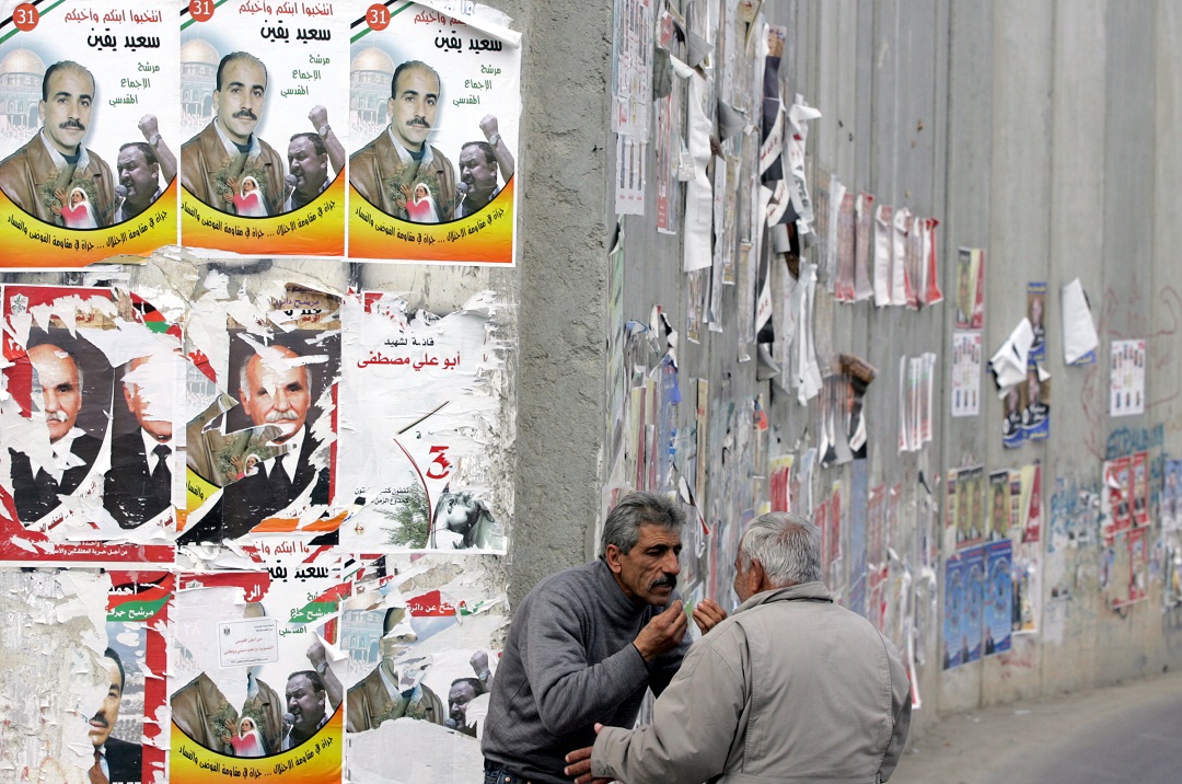 Des Palestiniens discutent près du mur de séparation israélien, tapissé d’affiches électorales palestiniennes, à Abu Dis, en périphérie de Jérusalem, le lendemain des législatives palestiniennes, le 26 janvier 2006 (AFP)