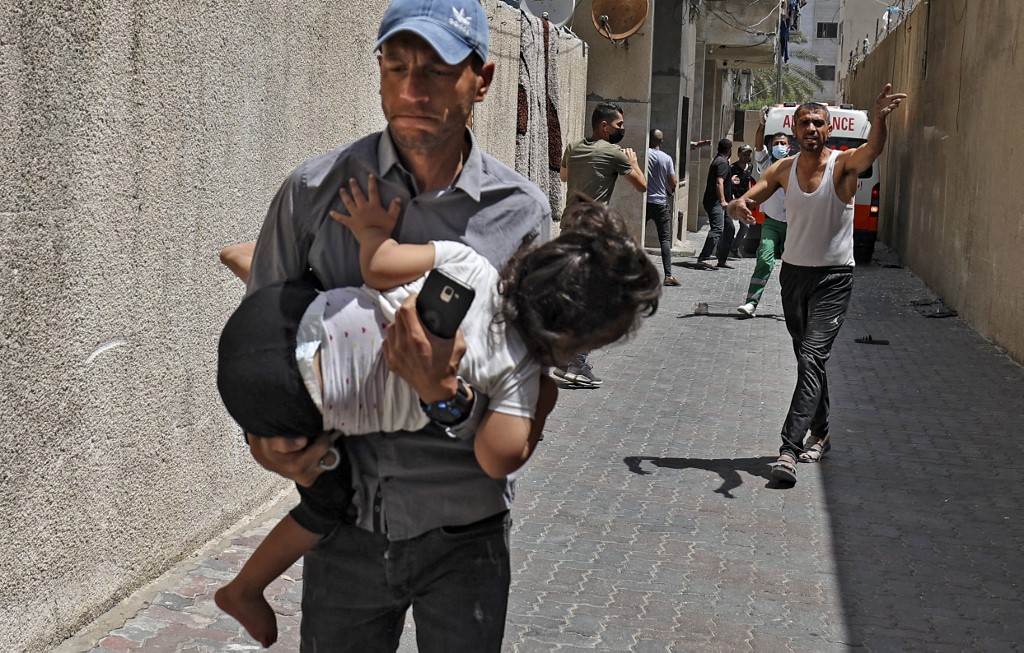 Un Palestinien s’enfuit devant les frappes israéliennes en tenant son fils contre lui, à Gaza, le 11 mai (AFP)