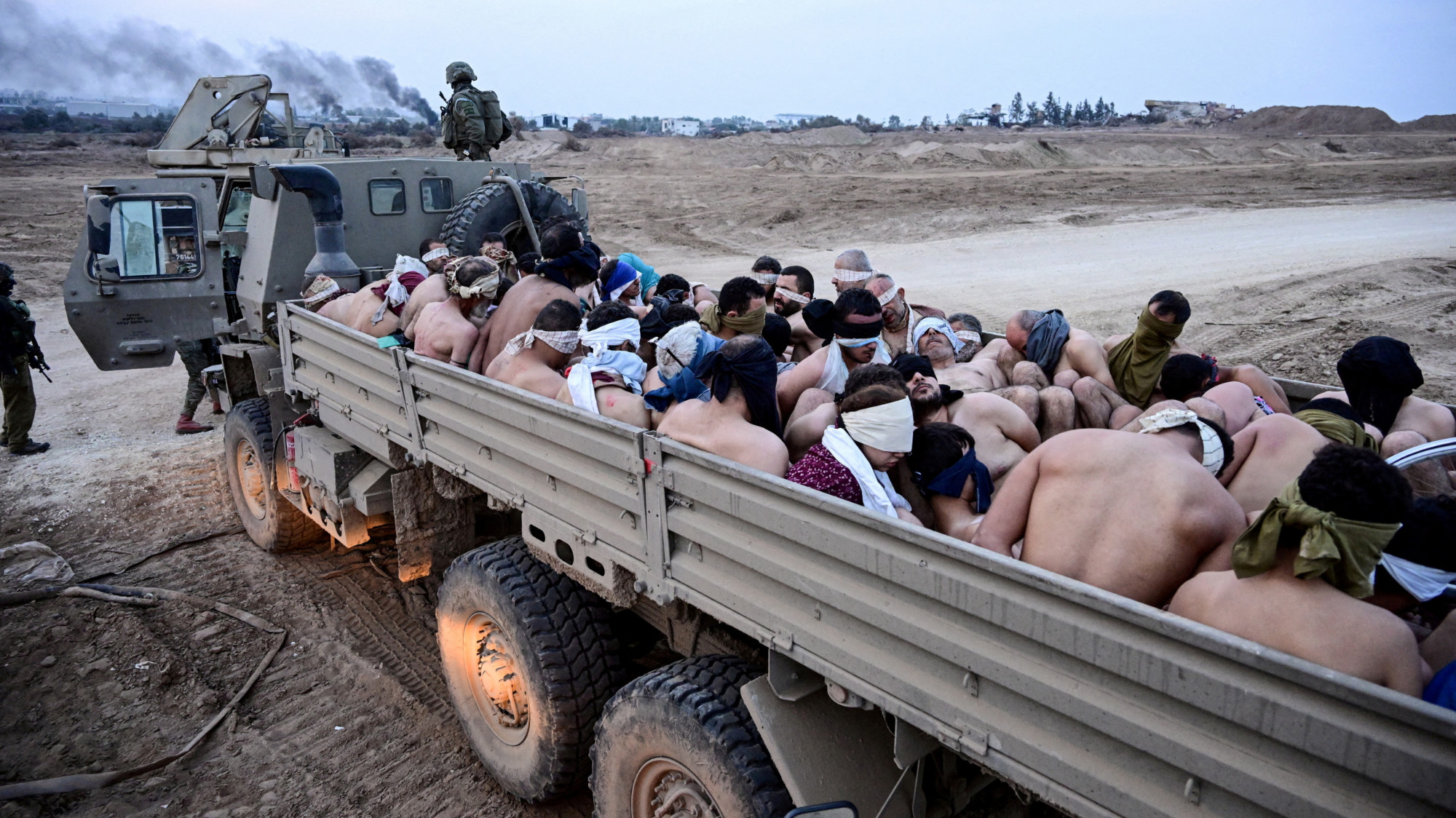 Israeli soldiers stand by a truck packed with shirtless Palestinian detainees in the Gaza Strip 8 December 2023 (Reuters/Yossi Zeliger)