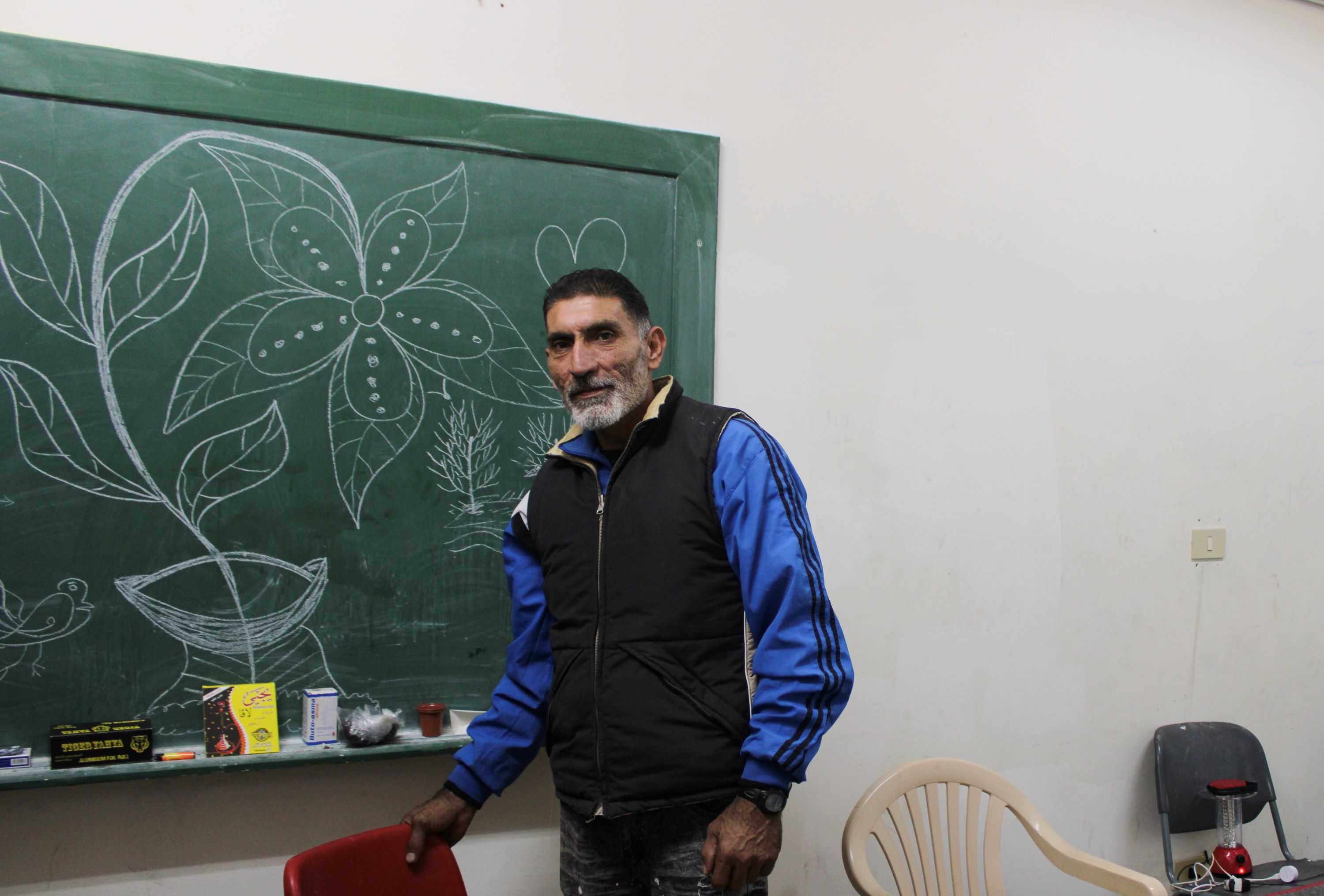 Joseph poses for a photo with his flowers in his room in the displacement shelter (Hanna Davis/MEE)