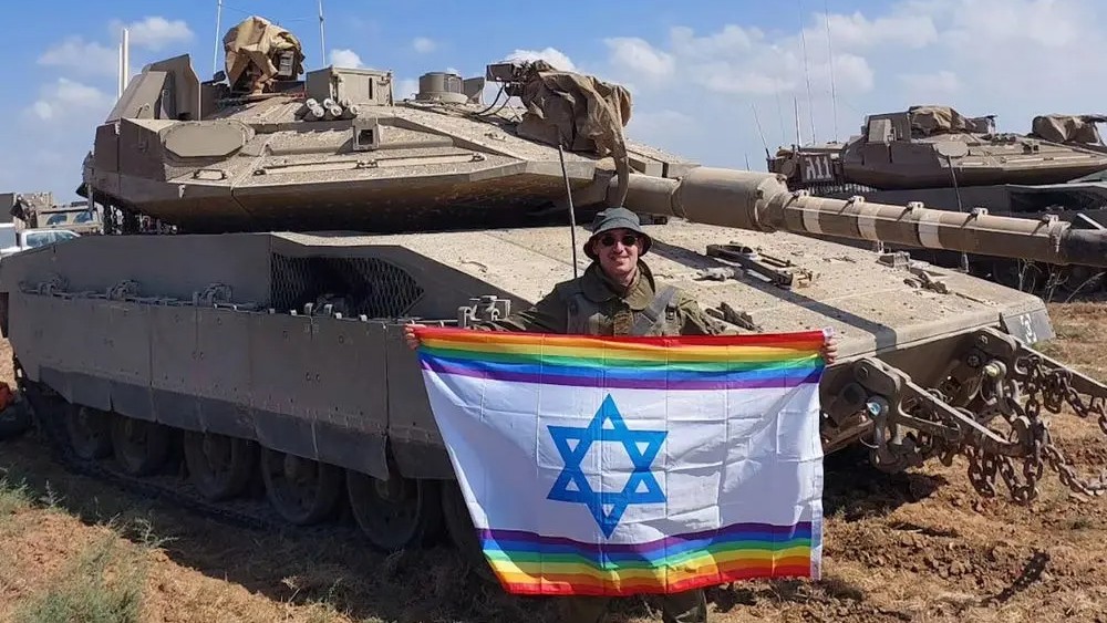 Yoav Atzmoni poses with an Israeli flag with rainbow colours next to a tank (social media)