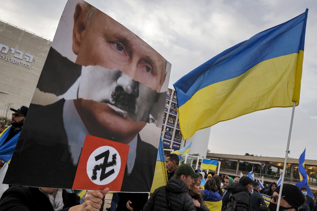 A demonstrator holds up a sign depicting Russian President Vladimir Putin as Adolf Hitler during a protest in Tel Aviv, Israel, 20 March 2022 (AFP)