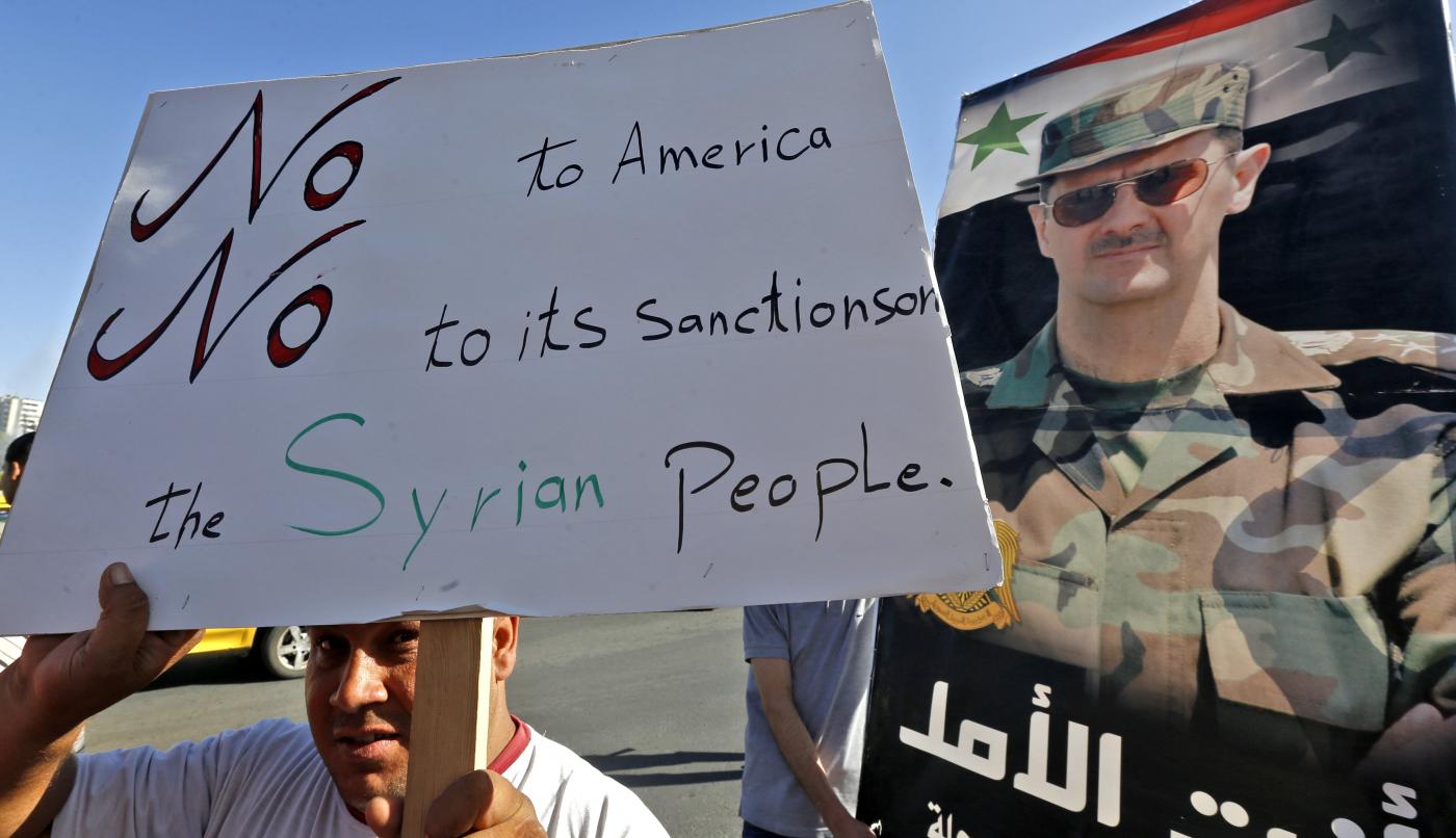 Man holds sign supportive of Syria's President Bashar al-Assad and critical of US sanctions in Damascus on 11 June (AFP)