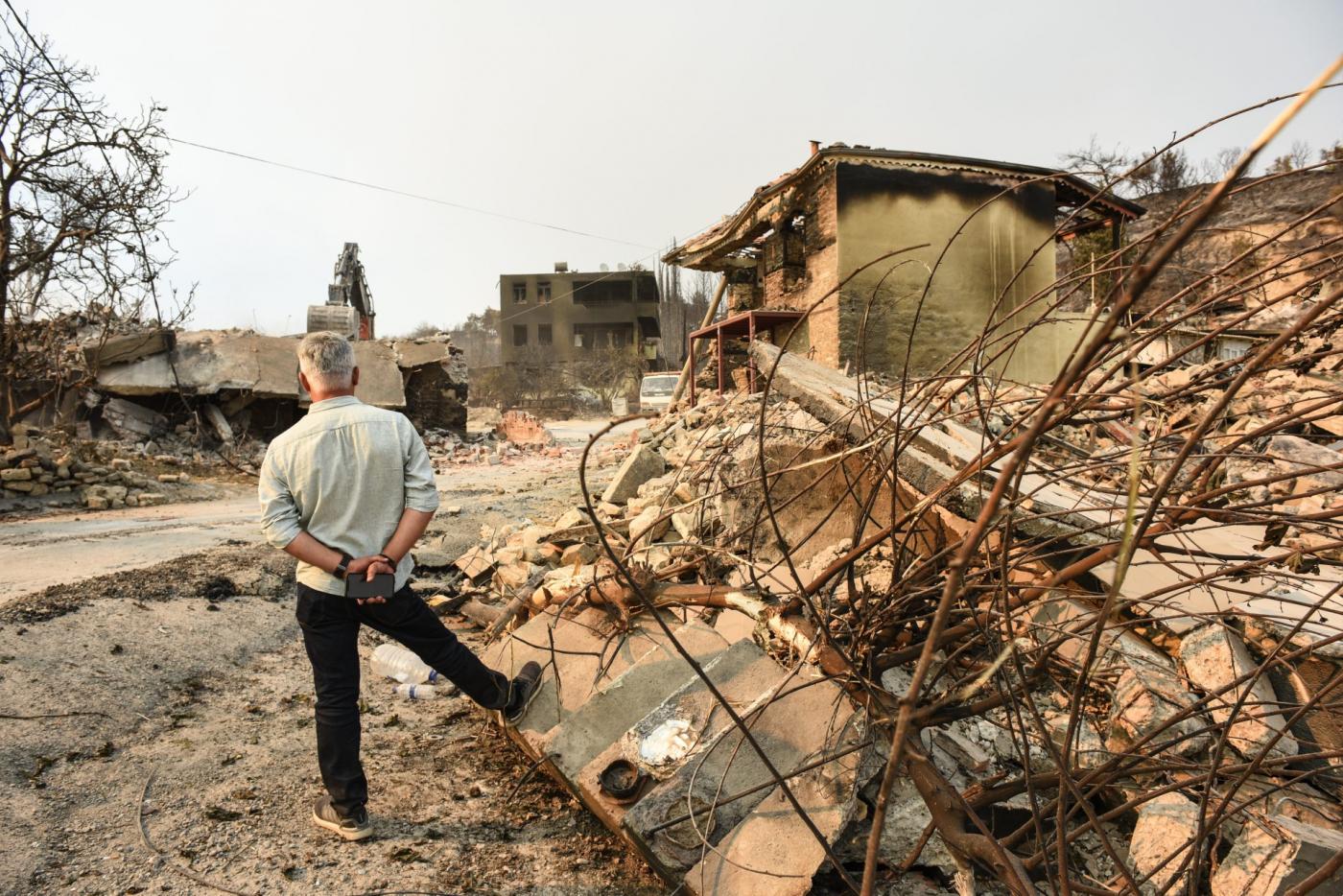 Un habitant se tient à côté des décombres de la maison d’un voisin et regarde les vestiges calcinés de sa propre maison (MEE/Yusuf Selman Inanc)