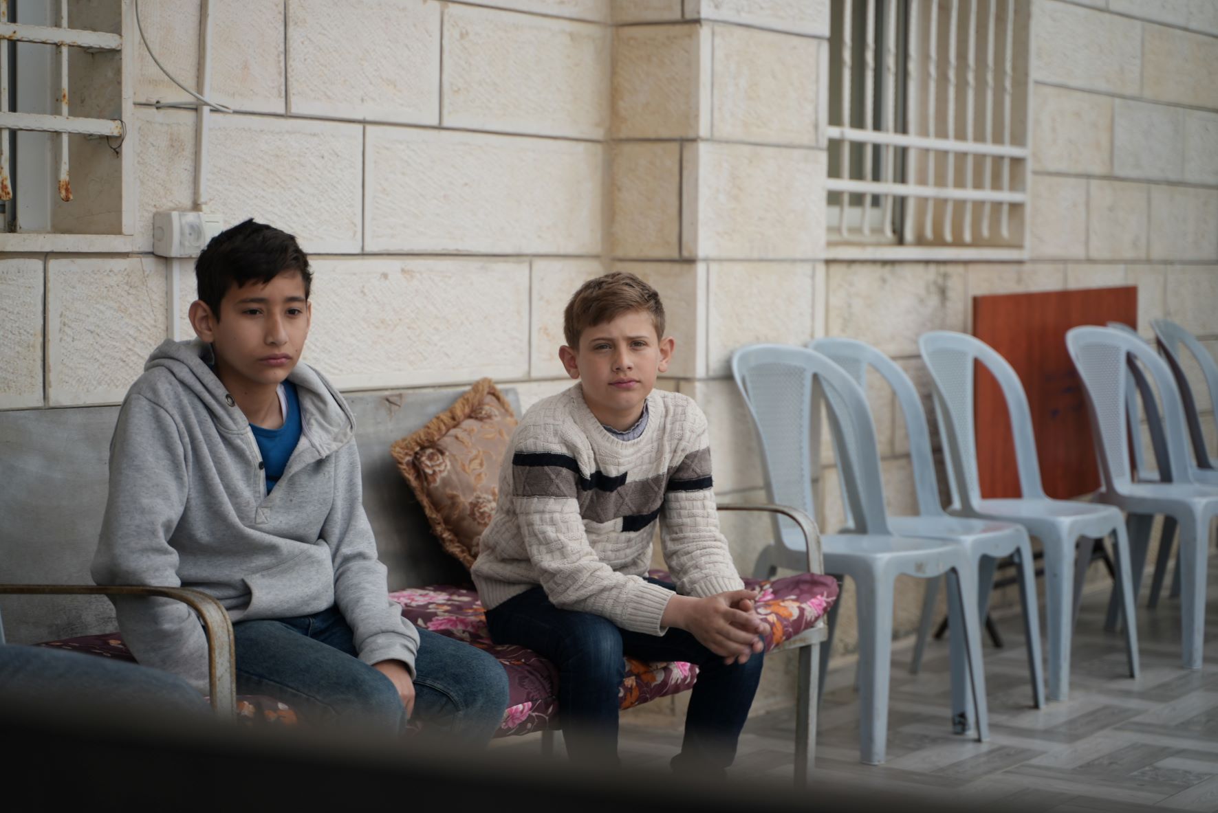 A son of Ghada Sabateen sits with a friend outside her house (Akram al-Waara)