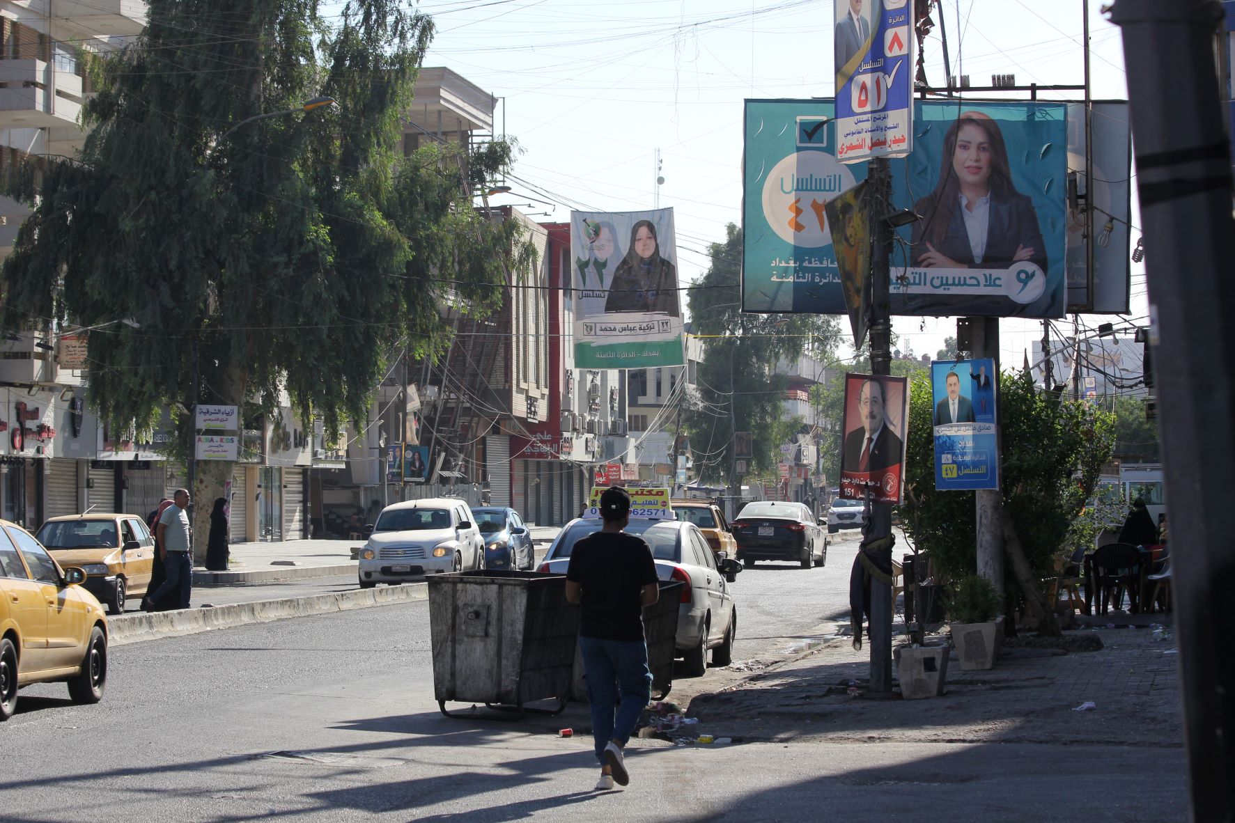 A man walks down a street in Karrada, Baghdad in October 2021 surrounded by election posters (MEE/Alex MacDonald)