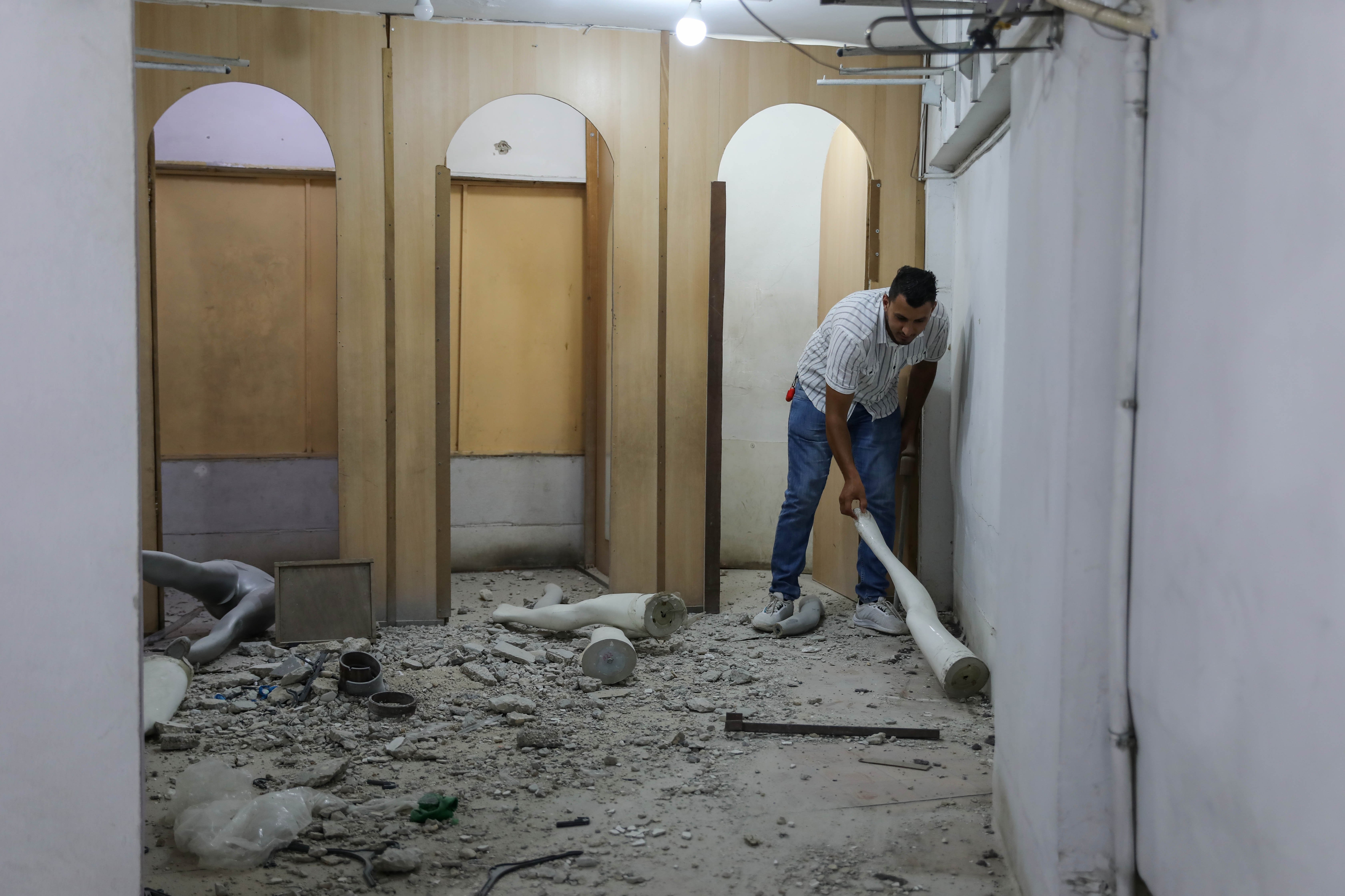 Un employé du magasin de vêtements de Taha Shurrab rassemble les morceaux d’un mannequin détruit par une bombe qui a touché le magasin sans exploser (MEE/Mohammad al-Hajjar)
