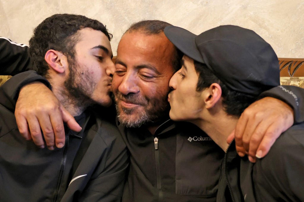 Palestinian brothers Qassam (L) and Nasrallah (R) reunite with their father Iyad al-Awar after both were released from an Israeli prison, at their home in east Jerusalem, 26 November 2023 (AFP)
