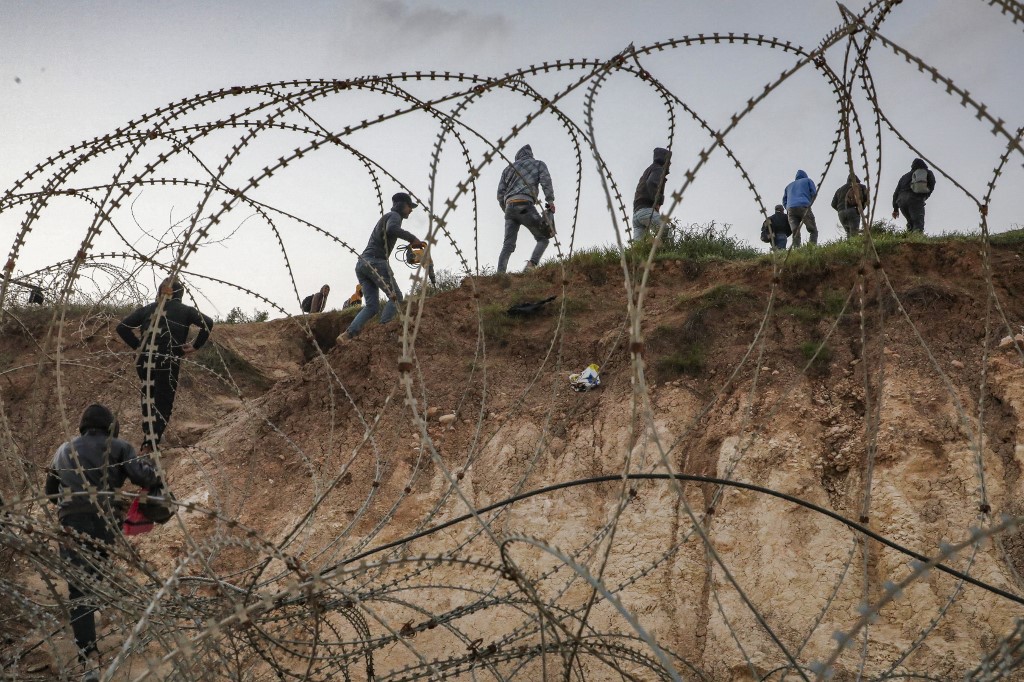 Palestinians go through a barbed-wire fence into Israel as they attempt to reach their workplaces close to the Israeli checkpoint of Mitar, near Hebron, occupied West Bank, 1 March 2021