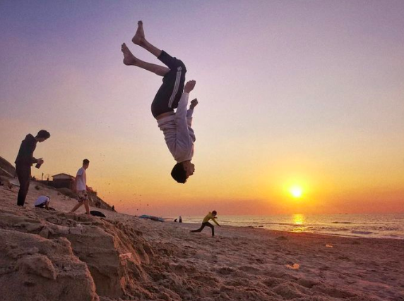 A Palestinian youth backflips onto a beach somewhere in Gaza as the sun sets.