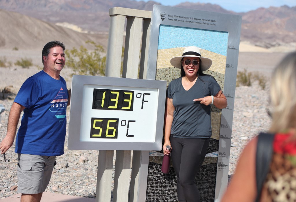 Tourists pose for a photo next to a digital display of a record heat in Death Valley, California, on 16 July 2023 (AFP)