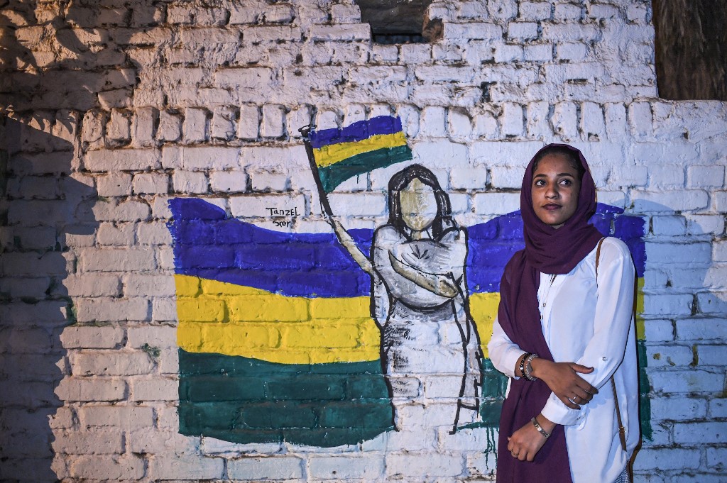 Demonstrator Alaa Salah poses by a mural of a female protester in Khartoum on 24 April (AFP)