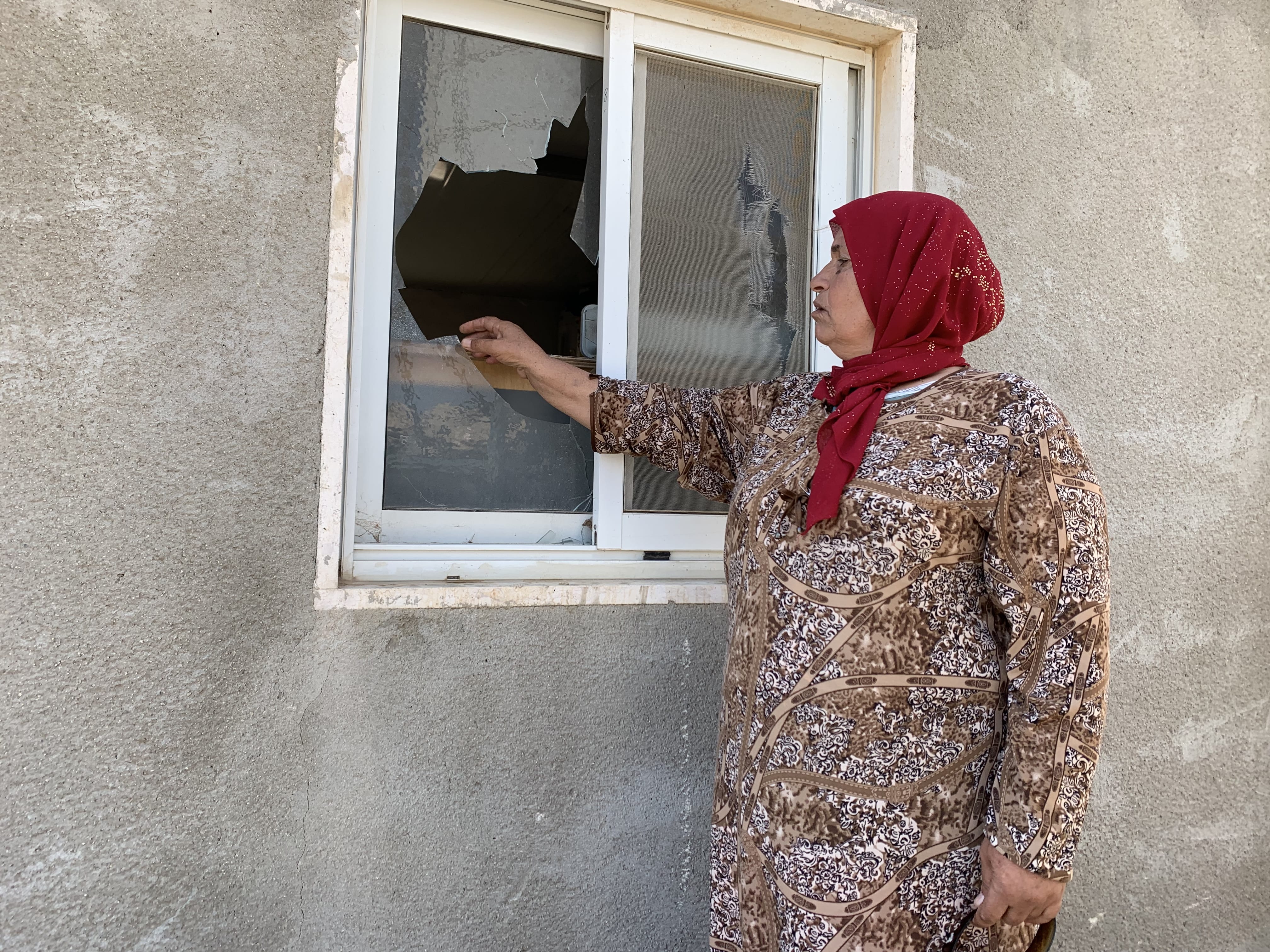 Rasmiyya Hammadah montre les fenêtres cassées de sa maison après une attaque de colons israéliens, le 3 octobre 2021 (MEE/Shatha Hammad)