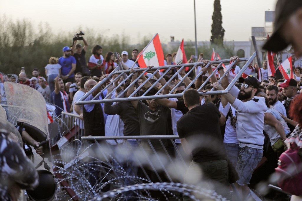 Lebanese demonstrators try to remove the barbed-wire and metal rail, placed by anti-riot police, on the road leading to the Presidential Palace in Baabda on Wednesday (AFP)