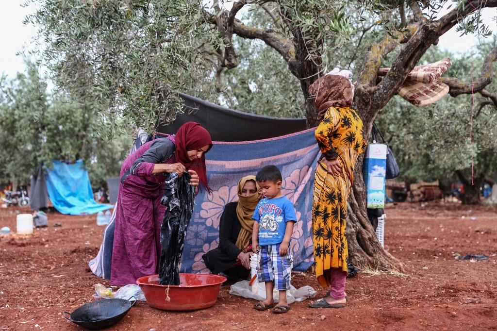 Displaced Syrian women wash clothes in a field in Idlib province on 23 May (AFP)