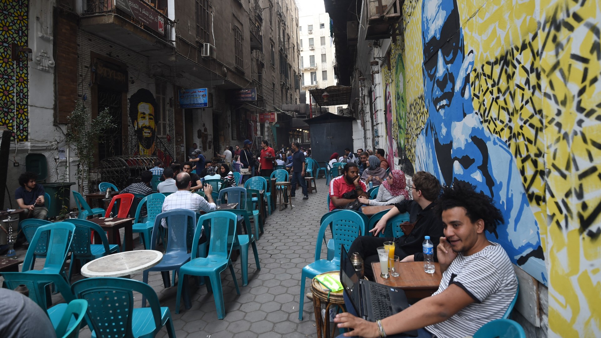 Egyptians gather at a cafe with graffiti on the walls bearing portraits of Egyptian footballer Mohamed Salah (L) and Nobel laureate Naguib Mahfouz (R), in central Cairo on 22 March, 2018 (AFP)