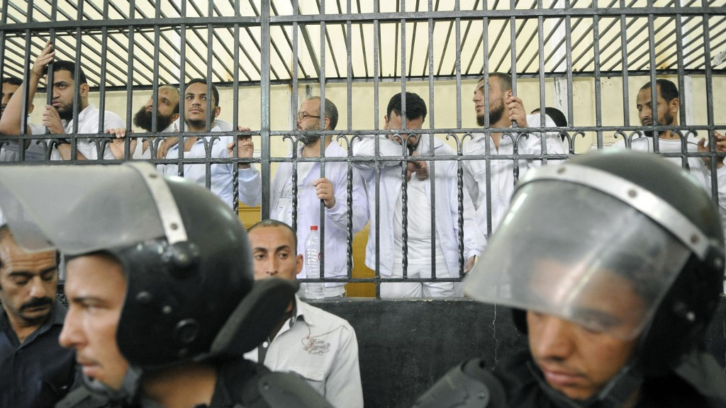 Police stand guard as Egyptians react from behind the defendant’s cage during their trial in May 2014 (AFP)