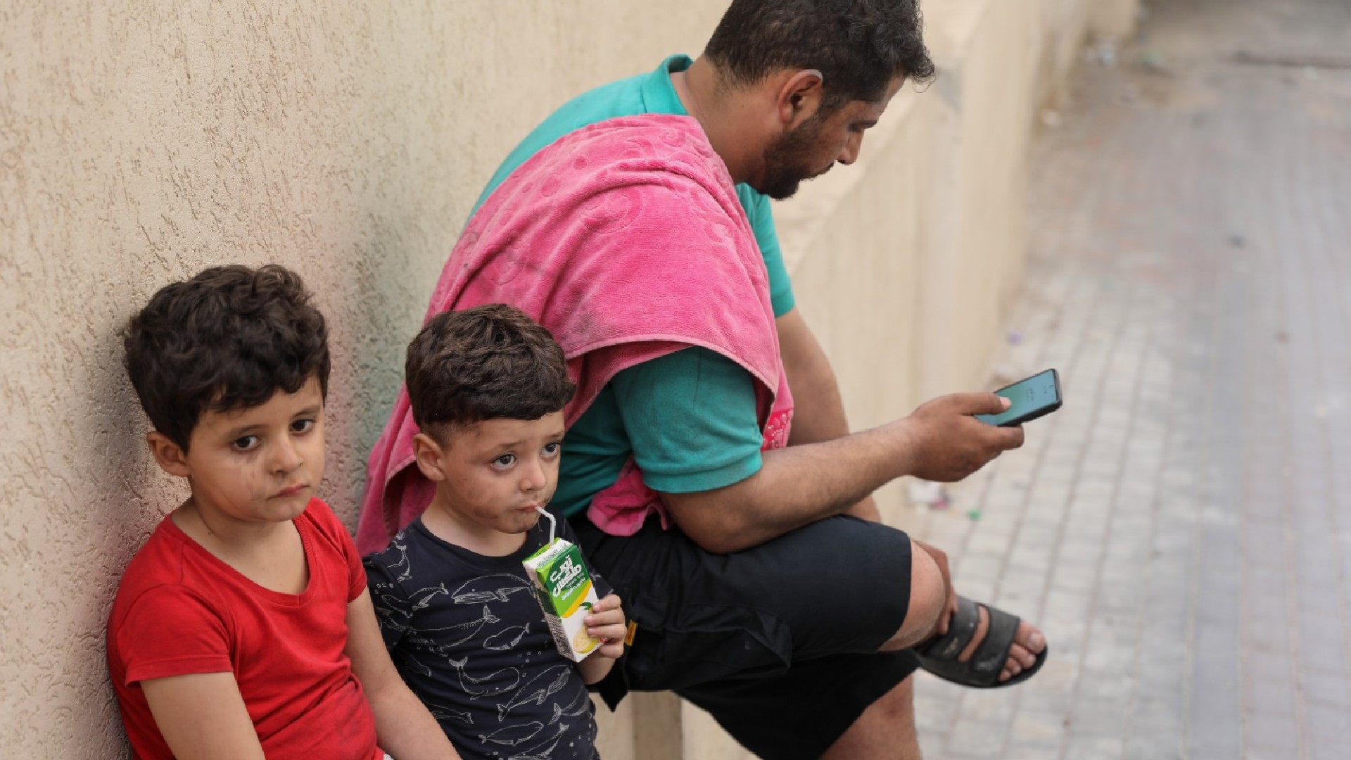 Khaled al-Hindi sheltering with his two children in a neighbour's home after the building they lived in was struck by an Israeli raid in central Gaza on 12 May 2023 (MEE/Mohammed al-Hajjar)