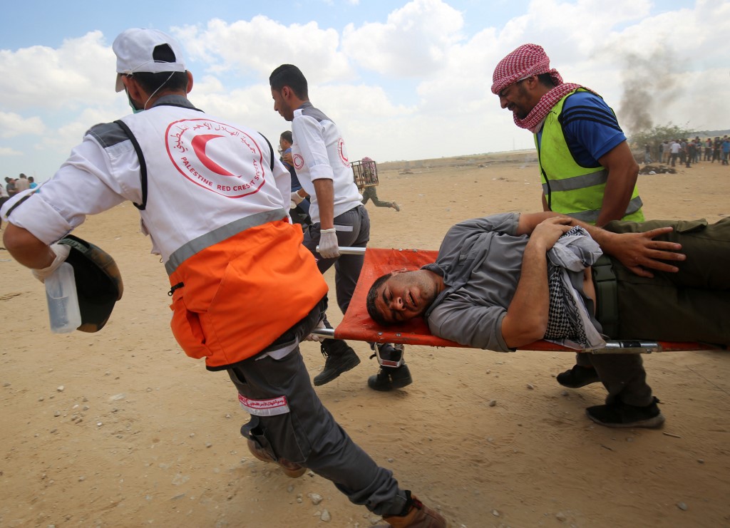 Palestinians carry a protester injured near the Gaza fence on 14 May 2018 (AFP)