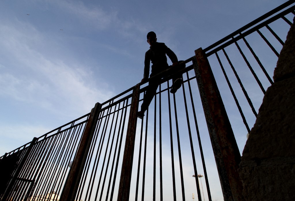 Un jeune garçon escalade une des clôtures de l’enclave espagnole de Melilla à la frontière du Maroc, le 16 mai 2017 (AFP/Antonio RUIZ)