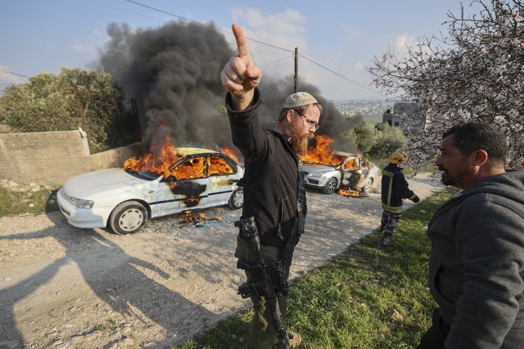 A member of security for the Israeli Bracha settlement gestures amid clashes between settlers and Palestinians in Burin village, occupied West Bank, after settlers reportedly set cars on fire there, 25 February 2023 (AFP)