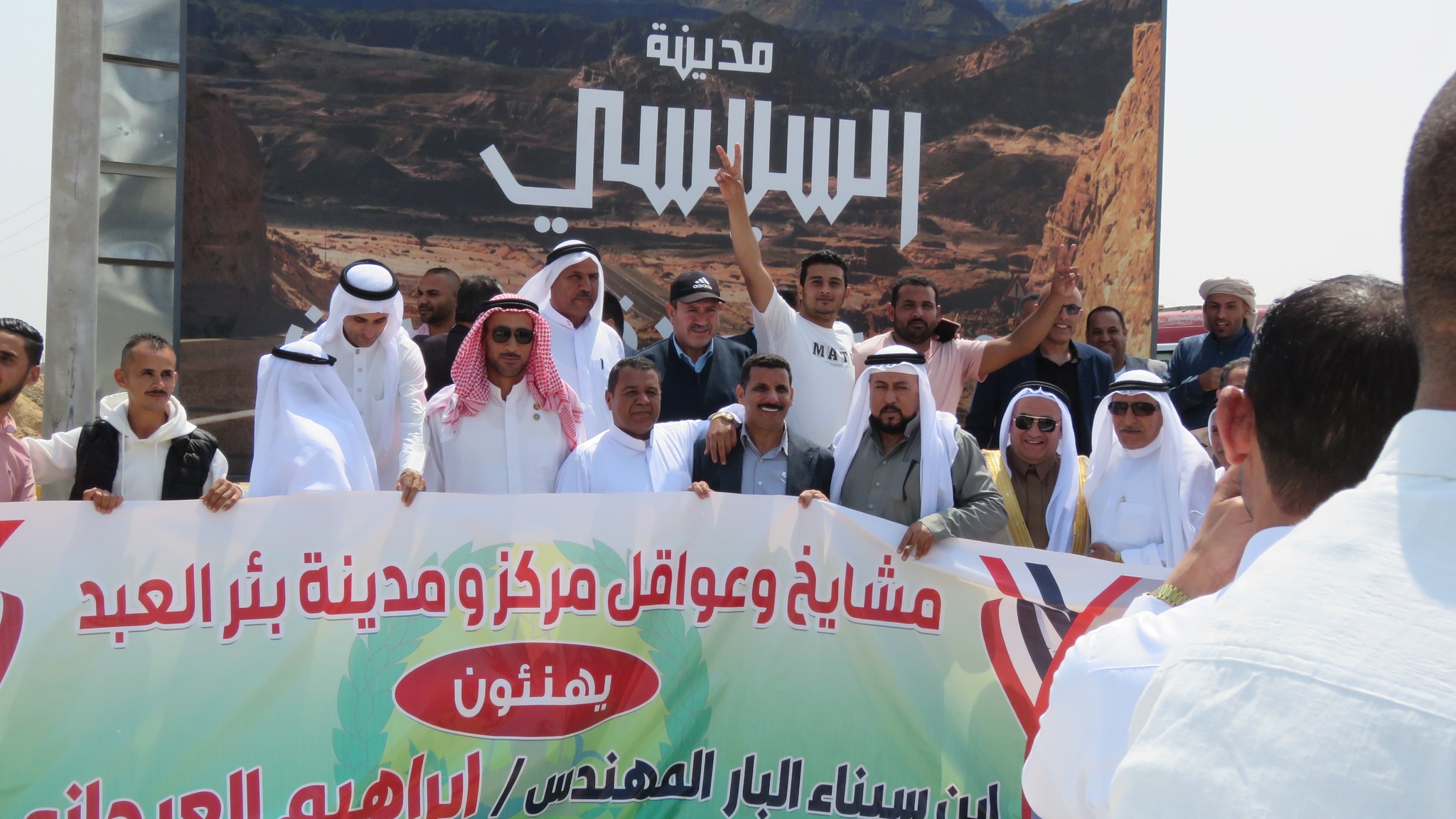 Sinai Bedouin figures carry a banner congratulating Organi for the new city, in front of a poster titled 'Sisi City', 1 May 2024 (Photo supplied to MEE)