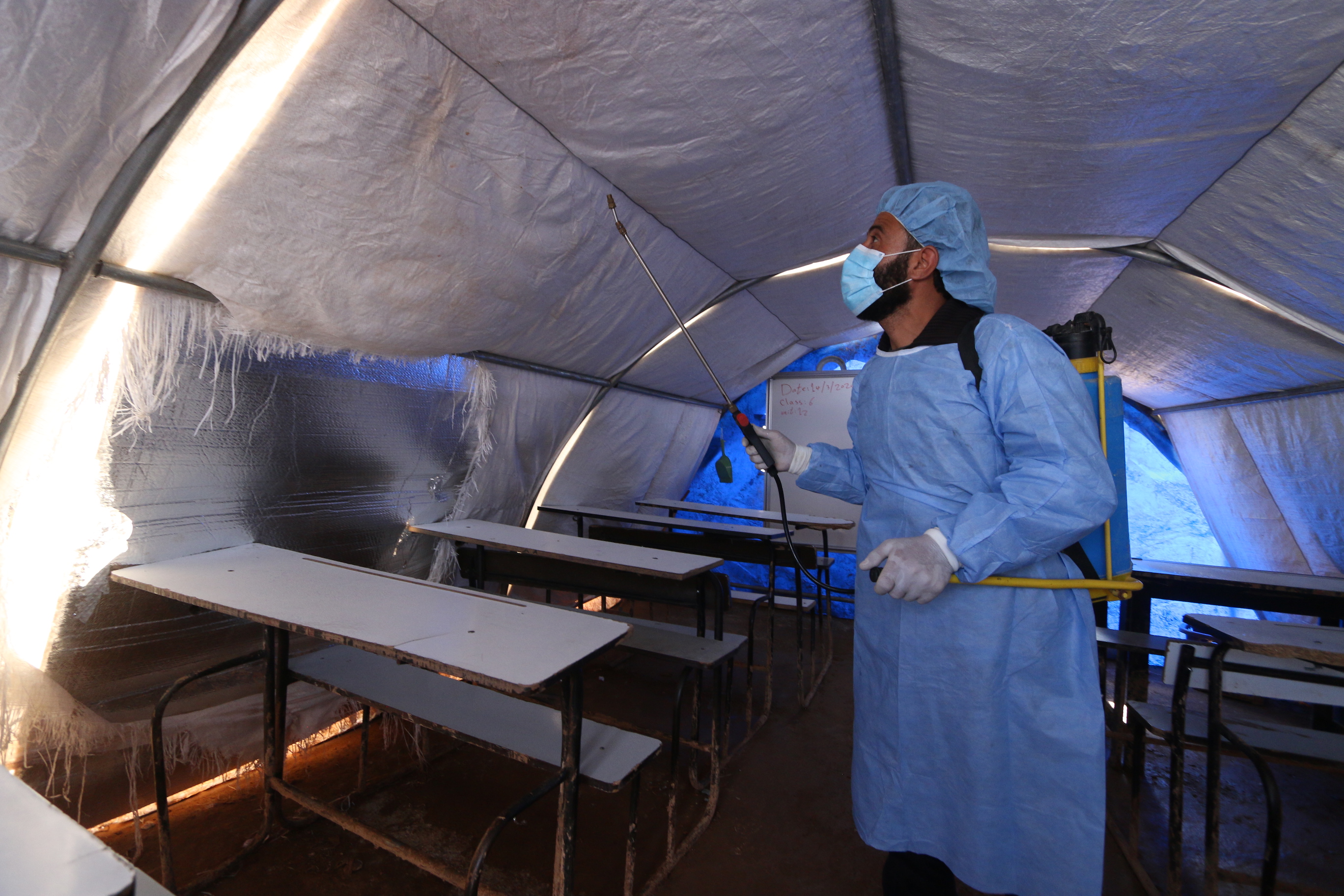 Aid workers in the Atmeh refugee camp sprayed disinfectant solution on surfaces to prevent spread of covid-19 (MEE/Yousef Gharib)