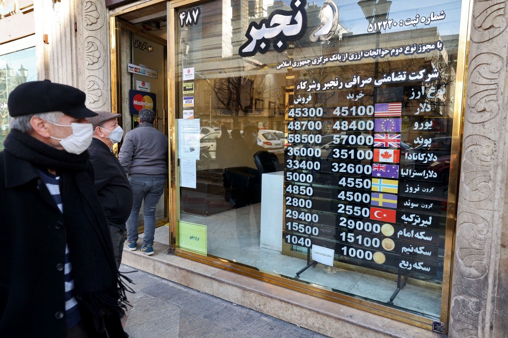 Men look at currency exchange rates at a shop in Tehran on 21 February 2023, as Iran’s currency recently plunged to new lows (AFP)