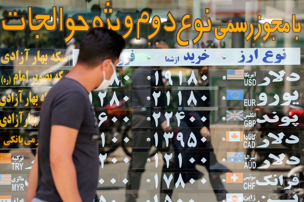 A man, wearing a protective mask due to the COVID-19 coronavirus, checks the currency exchange rates as he walks in the Iranian capital Tehran on June 22, 2020.  ATTA KENARE / AFP