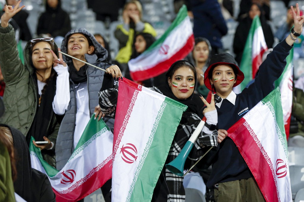 Women football fans wave Iranian national flags as they cheer for their national team during the friendly football match between Iran and Russia at Azadi Stadium in Tehran on March 23, 2023.