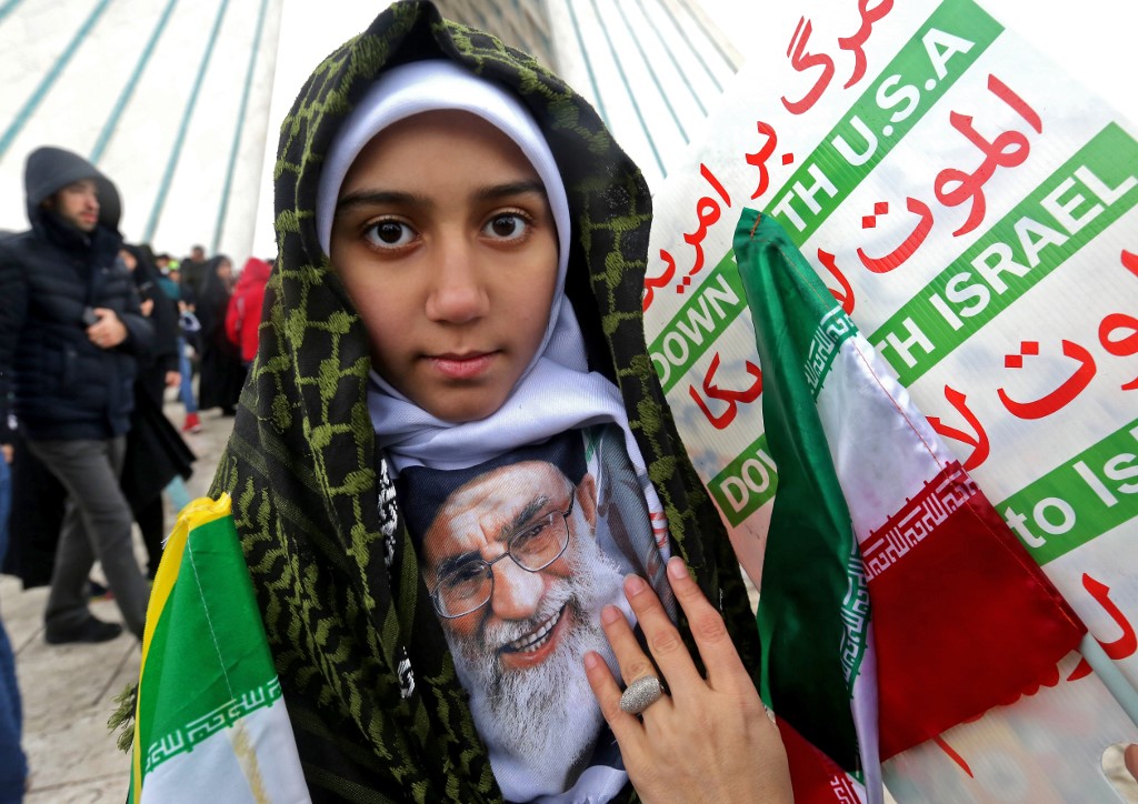 A girl poses with a portrait of Khamenei, alongside signs reading ‘Down with USA’ and ‘Down with Israel’, during celebrations for the revolution’s anniversary in Tehran on 11 February (AFP)