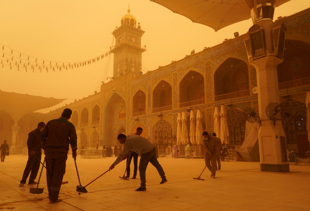 Volunteers clean up at the Imam Ali Shrine during a sandstorm in Najaf, Iraq, on 16 May 2022 (AFP)