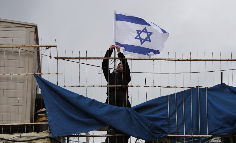 Settlers place an Israeli flag atop a Palestinian home in Jerusalem on 17 February (AFP)