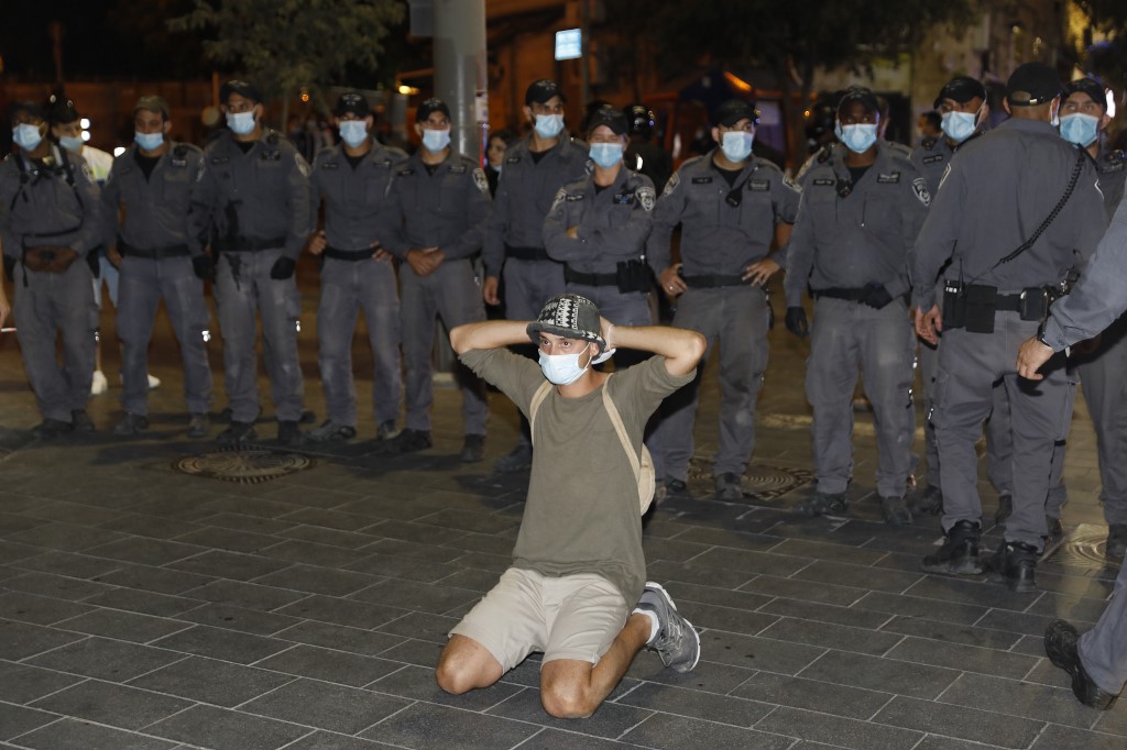 A protester kneels next to police in Jerusalem on 14 July (AFP)