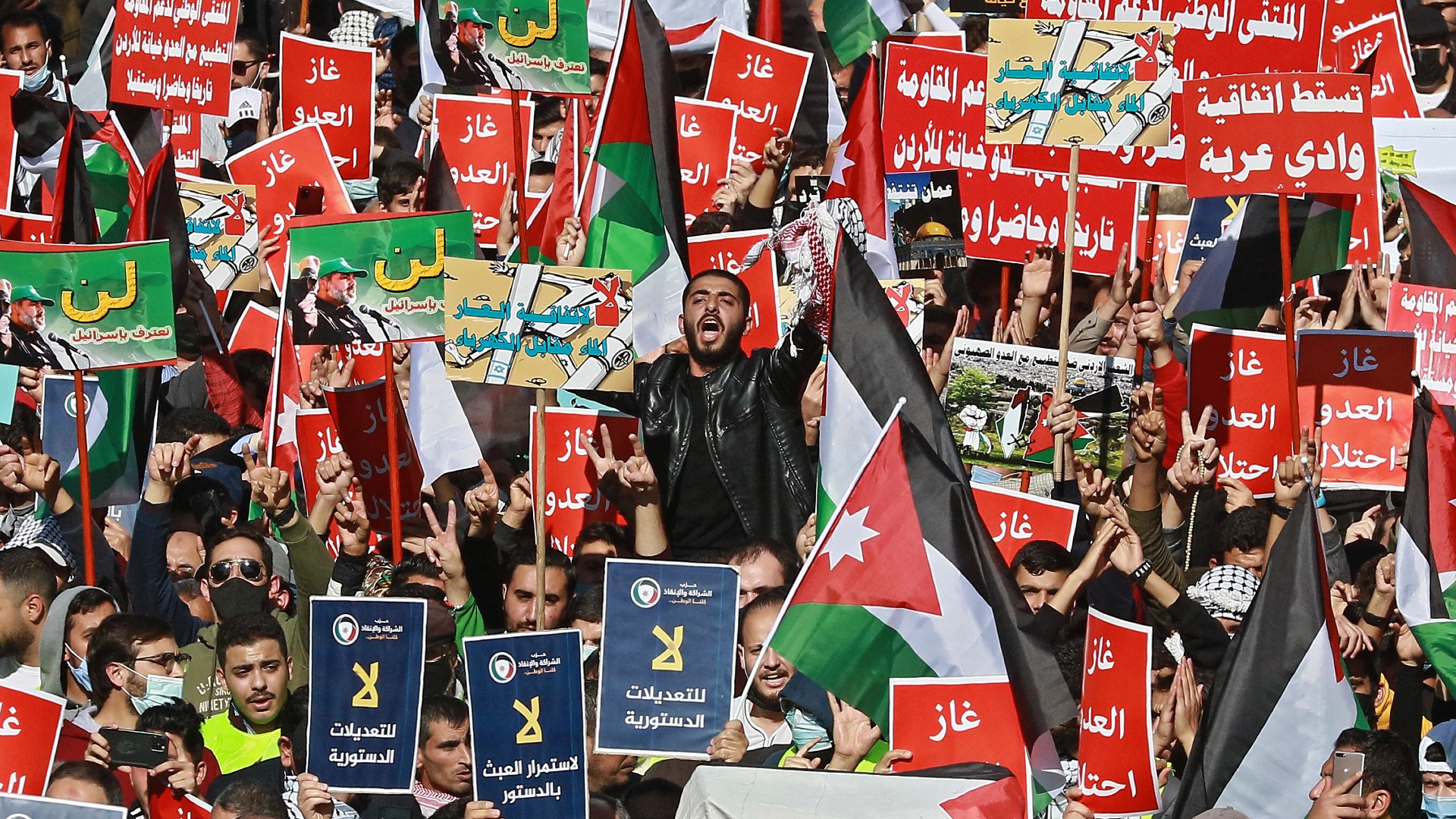 People hold up signs against agreements with Israel and others against constitutional amendment proposals, as hundreds of demonstrators gather in Jordan's capital Amman on November 26, 2021
